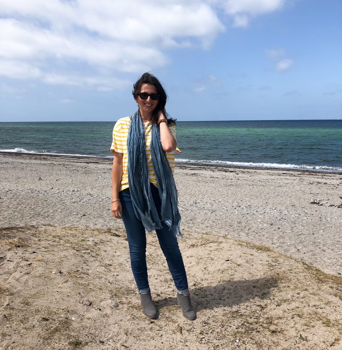 Erin stands on the beach along the Baltic Sea wearing a long scarf.