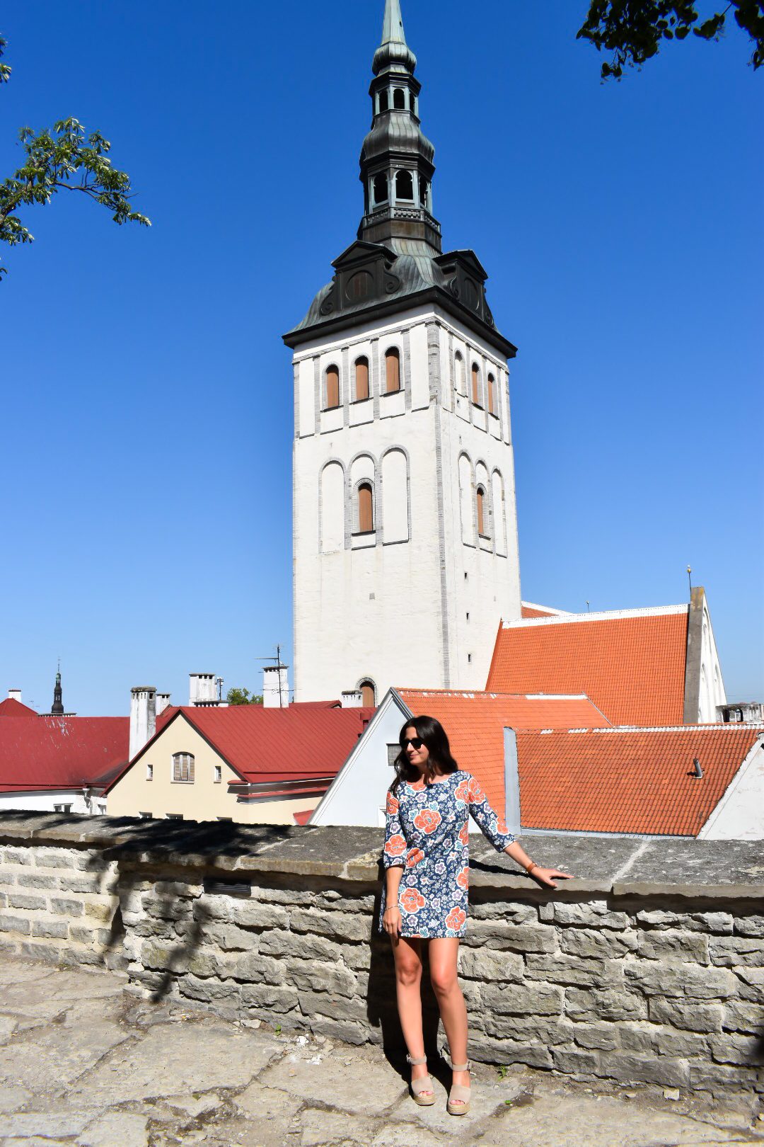 Erin leans against a stone wall in front of a tower in Tallinn Estonia