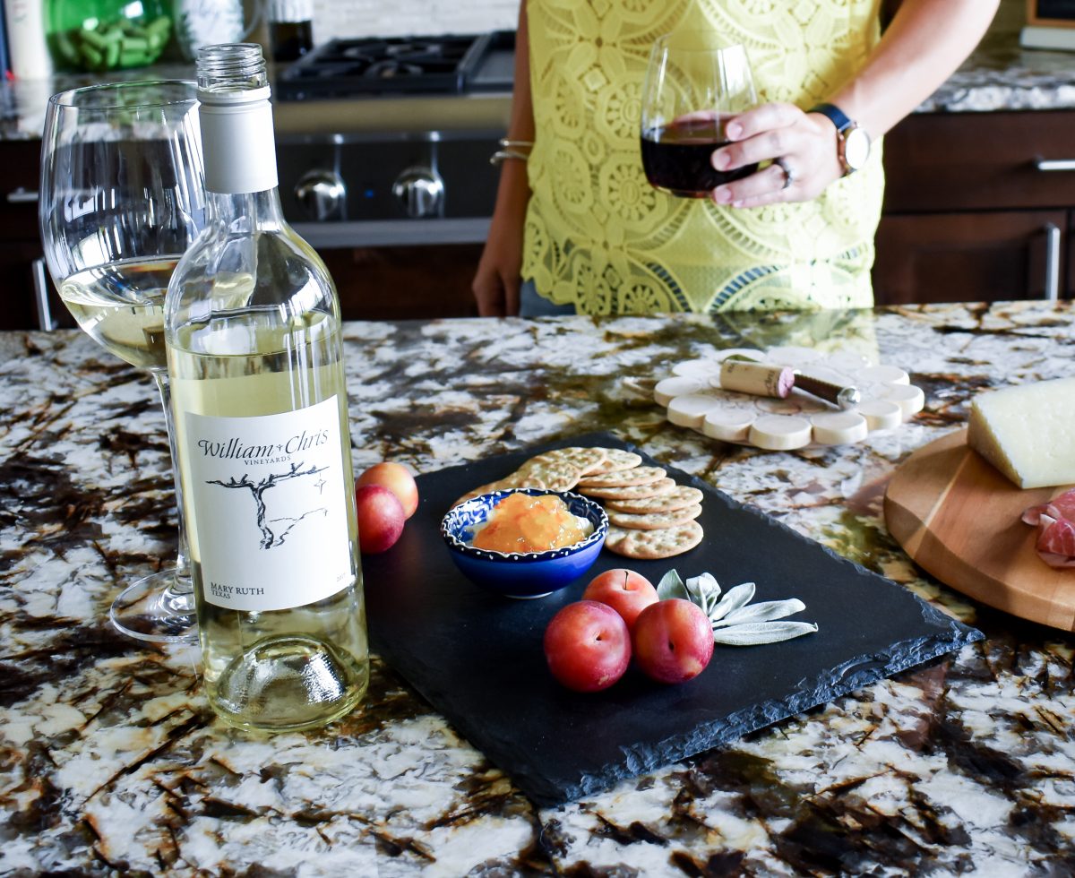 A cheese board with cherry plums, goat cheese, and pepper crackers with Mary Ruth white wine from William Chris Vineyards.