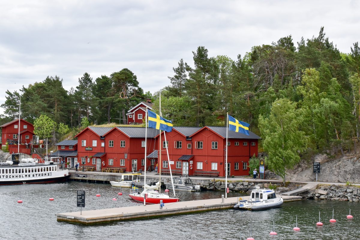 A view of red wooden buildings and Swedish flags along the archipelago